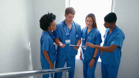 multi cultural medical team wearing scrubs meeting on stairs in hospital discussing patient chart