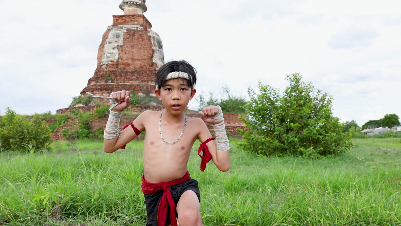 Anak laki-laki Asia menampilkan gerakan seni bela diri tradisional di luar ruangan dekat reruntuhan pagoda bata kuno