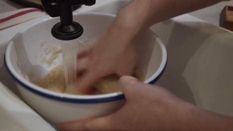 chef washes rice inside deep plate under the water in the sink