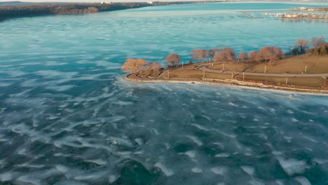 Aerial-shot-of-walking-trails-in-park-alongside-the-frozen-lake