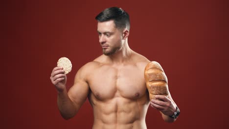 healthy food choices. naked sportsman choosing between healthy and unhealthy bread for his muscular body. portrait of handsome bodybuilder with bread in studio.