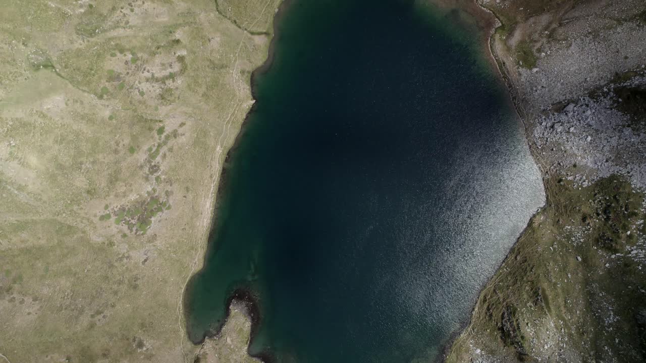 4K ascending top-down drone shot over Ibón de Acherito in the Western Valleys Natural Park, Aragonese Pyrenees, Spain. A stunning aerial view of the alpine lake and surrounding mountains.