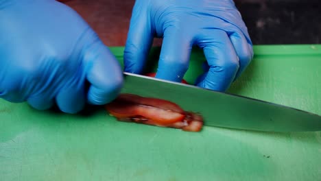 hands in gloves cutting tomato slice into strips, professional worker preparing food