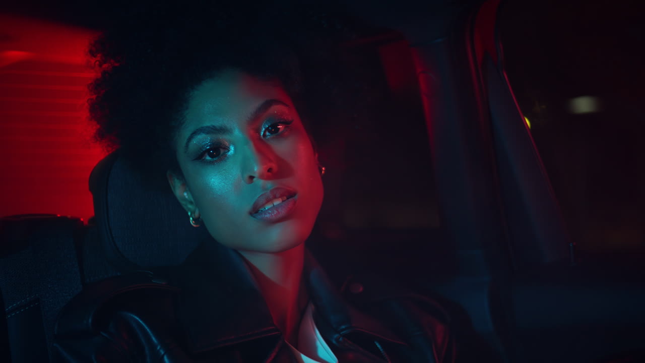 Modella affascinante seduta sul sedile posteriore dell'auto che guarda la fotocamera durante un viaggio notturno, primo piano
