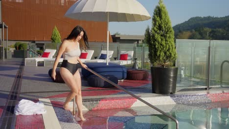 Sexy-slim-Asian-lady-with-brown-hair-in-swimsuit,-taking-robe-off-and-going-in-swimming-pool