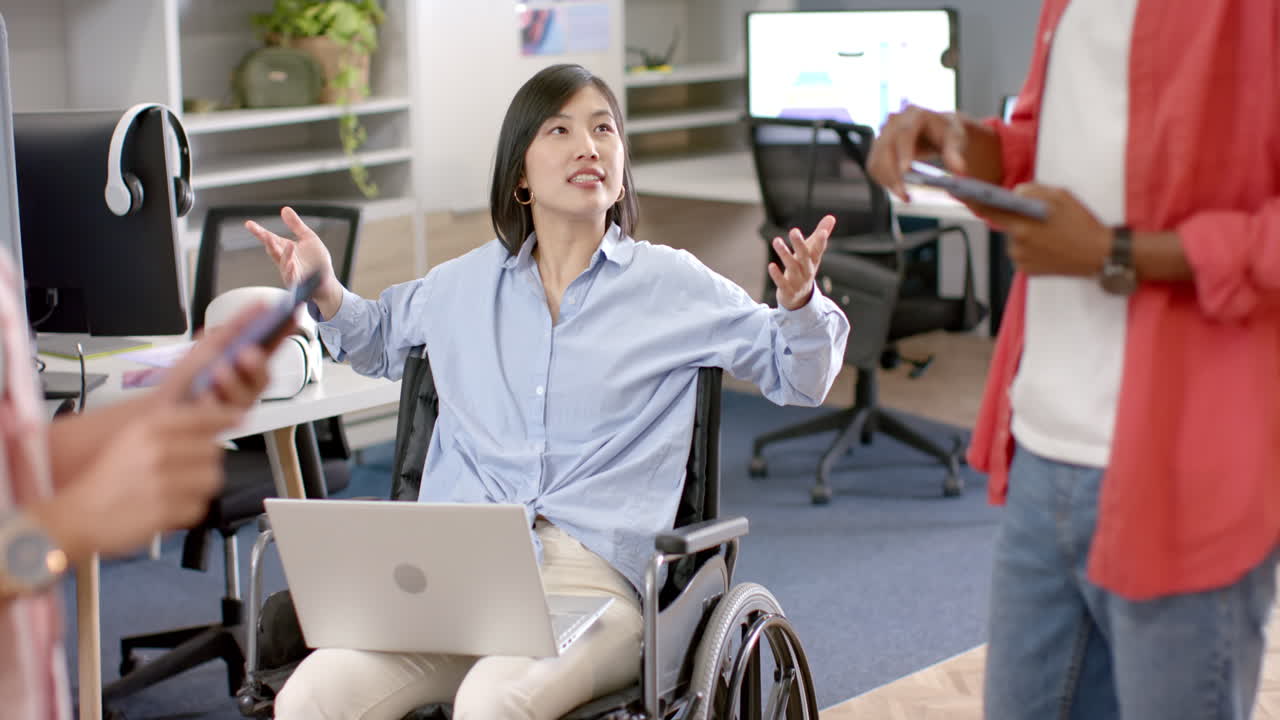 Discussing ideas, woman in wheelchair with laptop engaging with colleagues in office