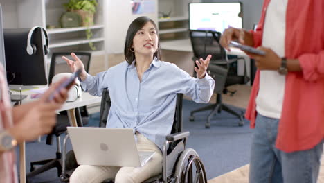 discussing ideas, woman in wheelchair with laptop engaging with colleagues in office