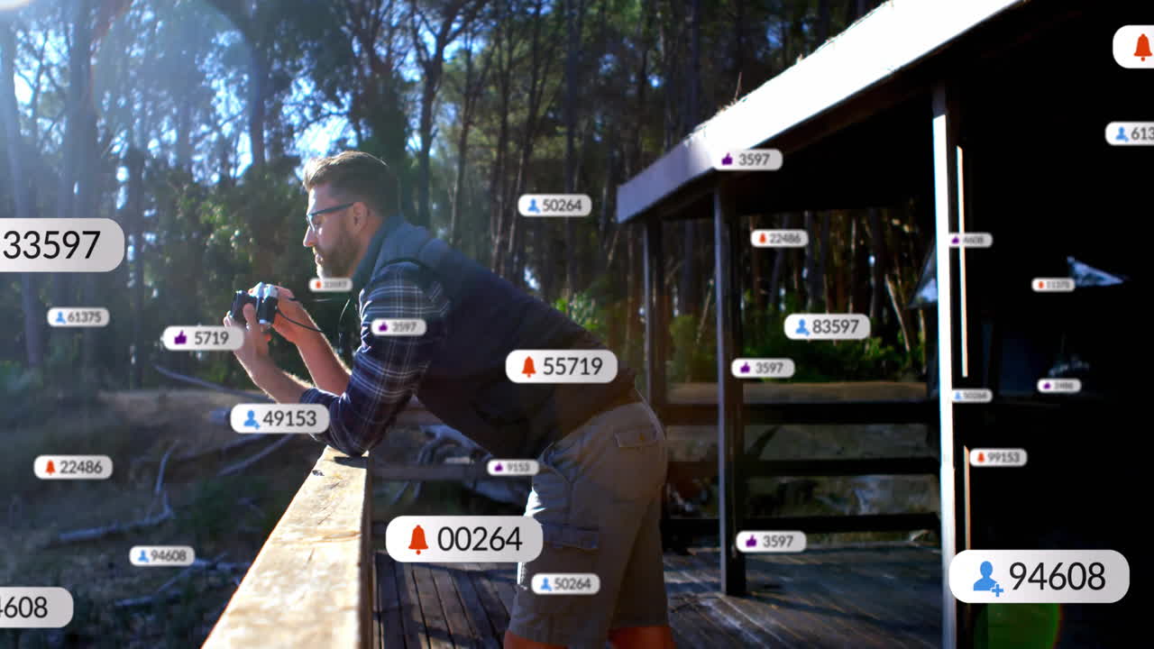 Man leaning on wood railing with camera capturing forest with floating social media marketing icons
