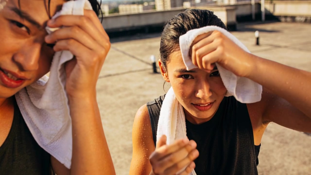 Wiping sweat post-workout, man and woman in black tank tops holding white towels on rooftop cooling