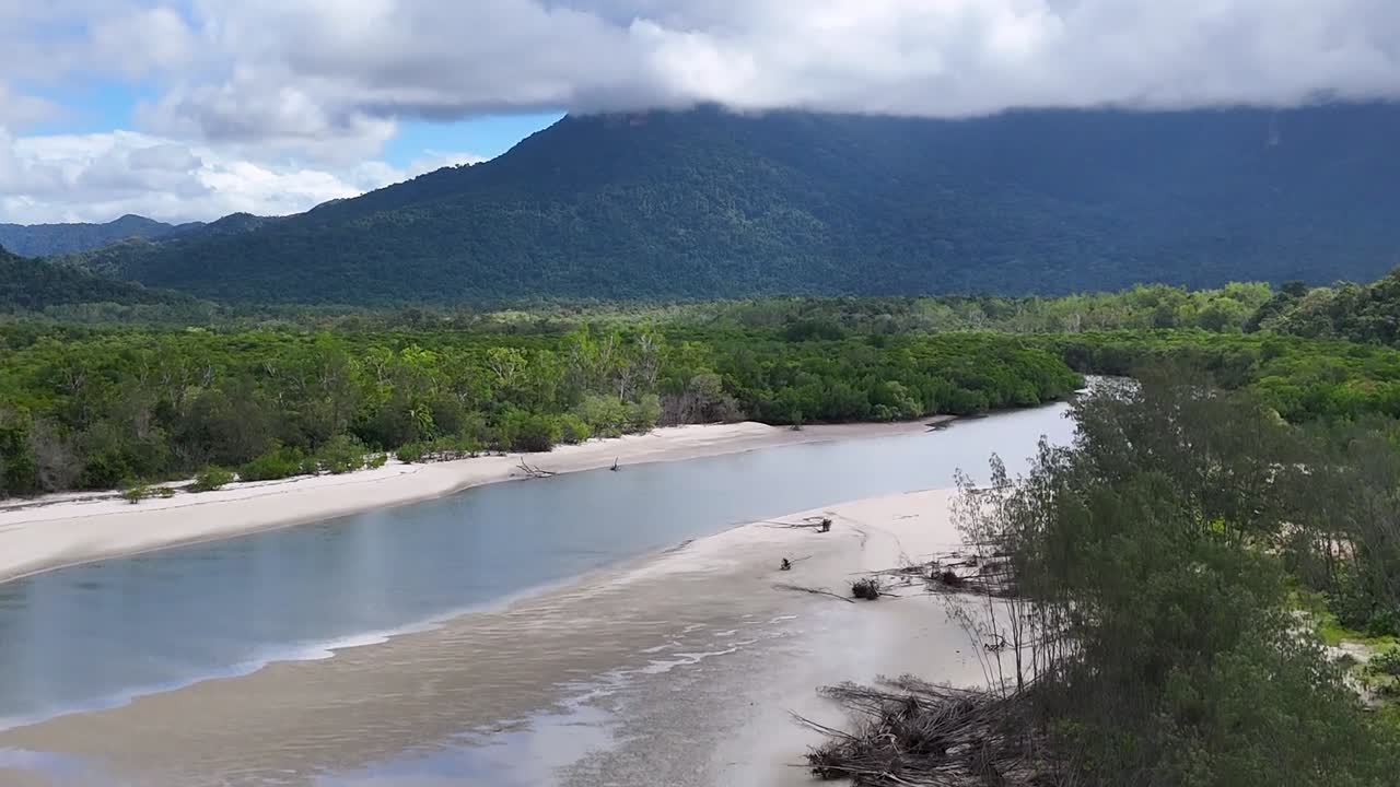 Drohnenaufnahmen zeigen einen sich schlängelnden tropischen Fluss mit sandigen Ufern, üppigem Regenwald und fernen Bergen.