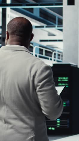 vertical video employee walking in server farm, analyzing equipment metrics on device screen