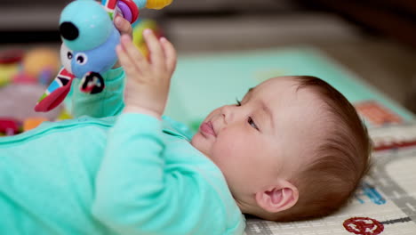 adorable healthy caucasian kid in blue clothes lies on his back. active baby waving his toy in the air. close up. blurred backdrop.