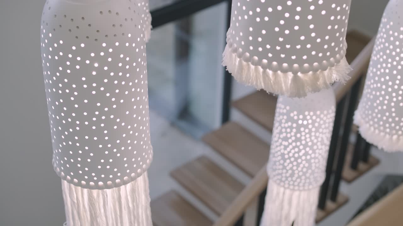 una serie de elegantes luces colgantes cilíndricas con una luz en cascada de patrón punteado a través de sus perforaciones, creando un ambiente lúdico y encantador en una escalera moderna