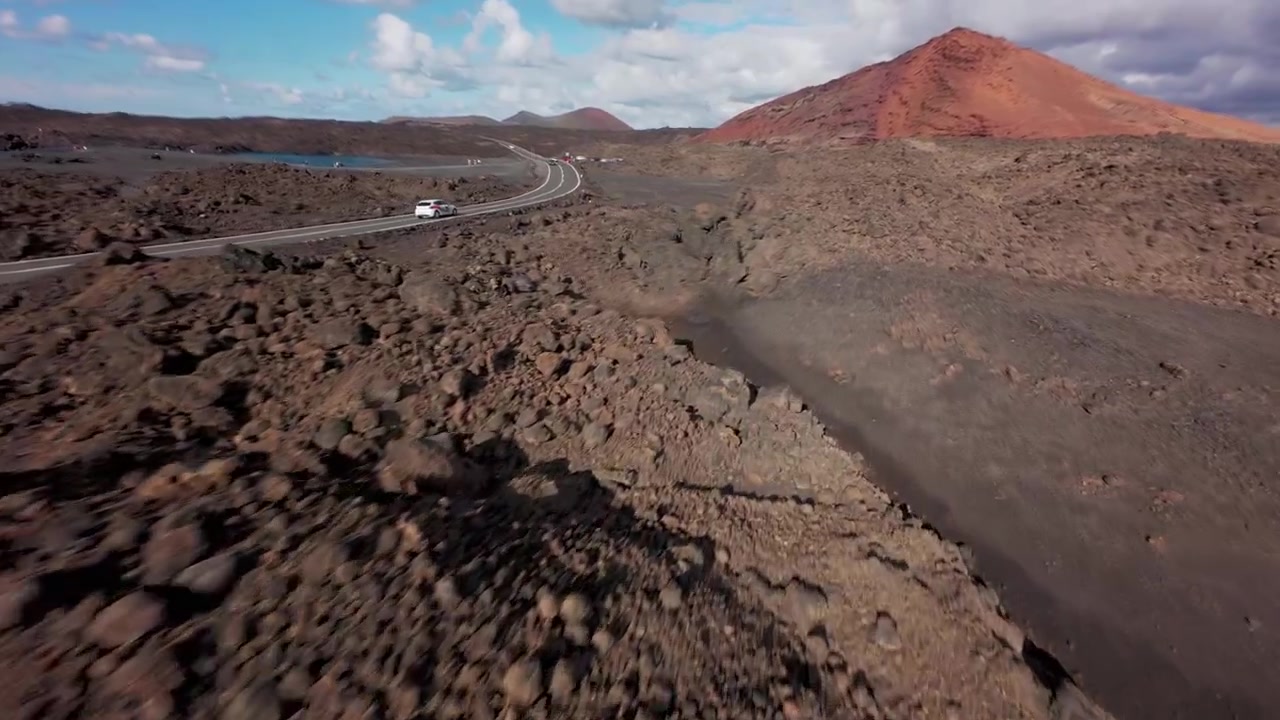 Volo di drone FPV che sorvola un campo di lava nera e accidentato vicino alla strada nel paesaggio vulcanico di Lanzarote, Spagna