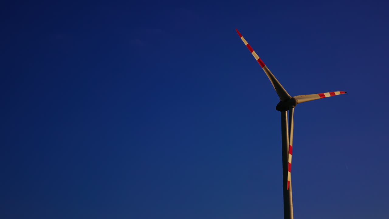 Wind turbine against a clear blue sky. A large wind turbine stands tall under a clear blue sky, displaying its blades prominently during the day