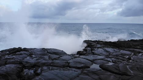 gliding slow motion drone shot travelling out over cliff edge of old lava flow as waves crash against the cliffs causing spray and surf