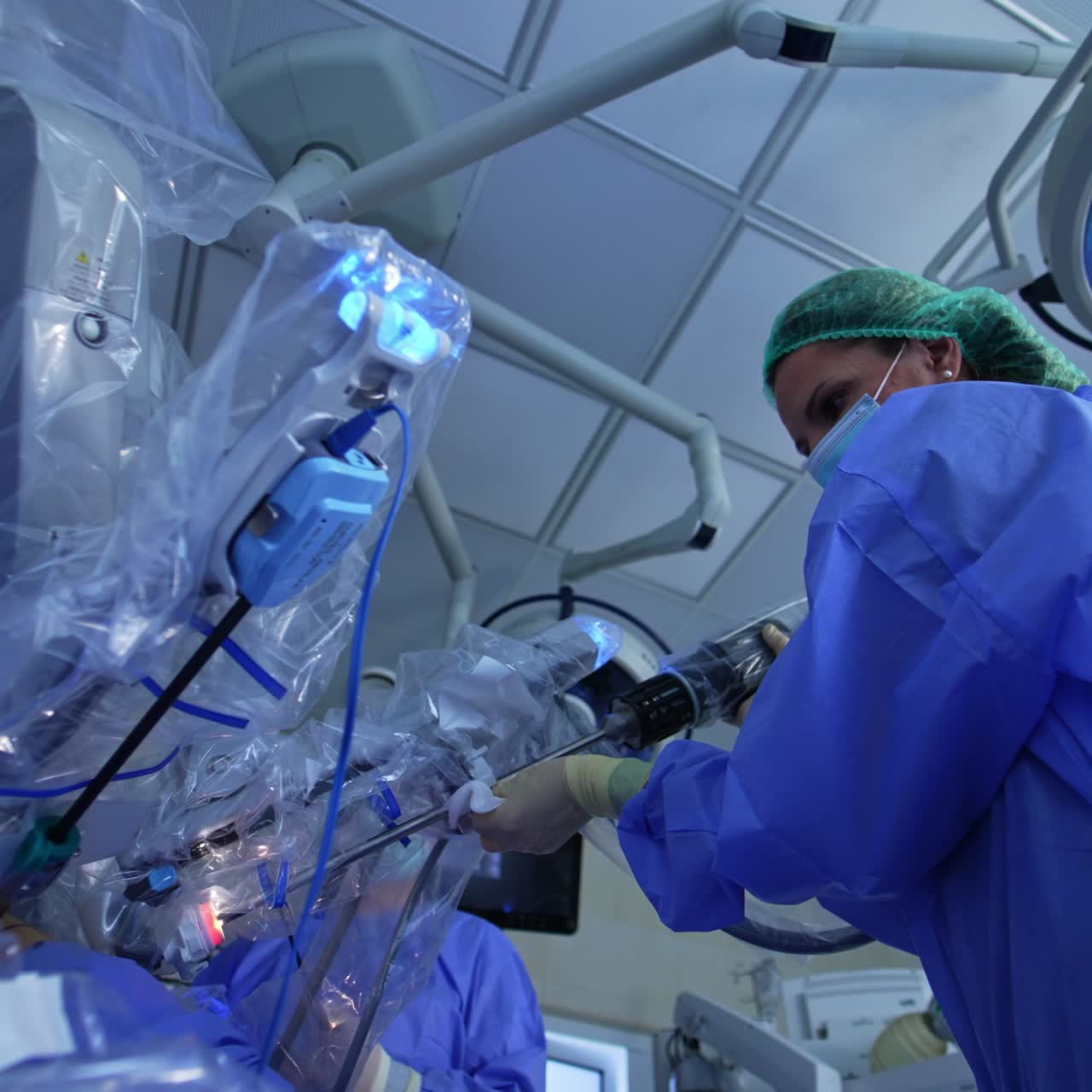 First assistant takes the robotic arm of Da Vinci robot, wipes it with a napkin and attaches to the joint. Low angle view