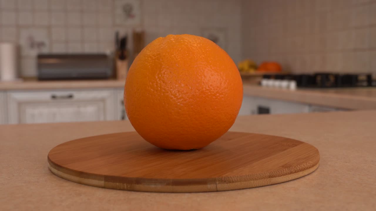 un primer plano de una fruta de naranja entera. una cámara giratoria con una cocina blanca en el fondo.