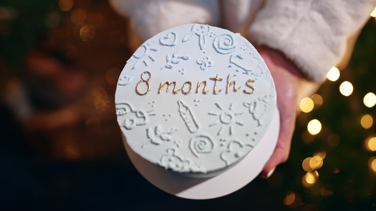 Beautiful white cake with pictures and a sign "eight months" in female hands. Celebrating the first months of child's life. Close up.