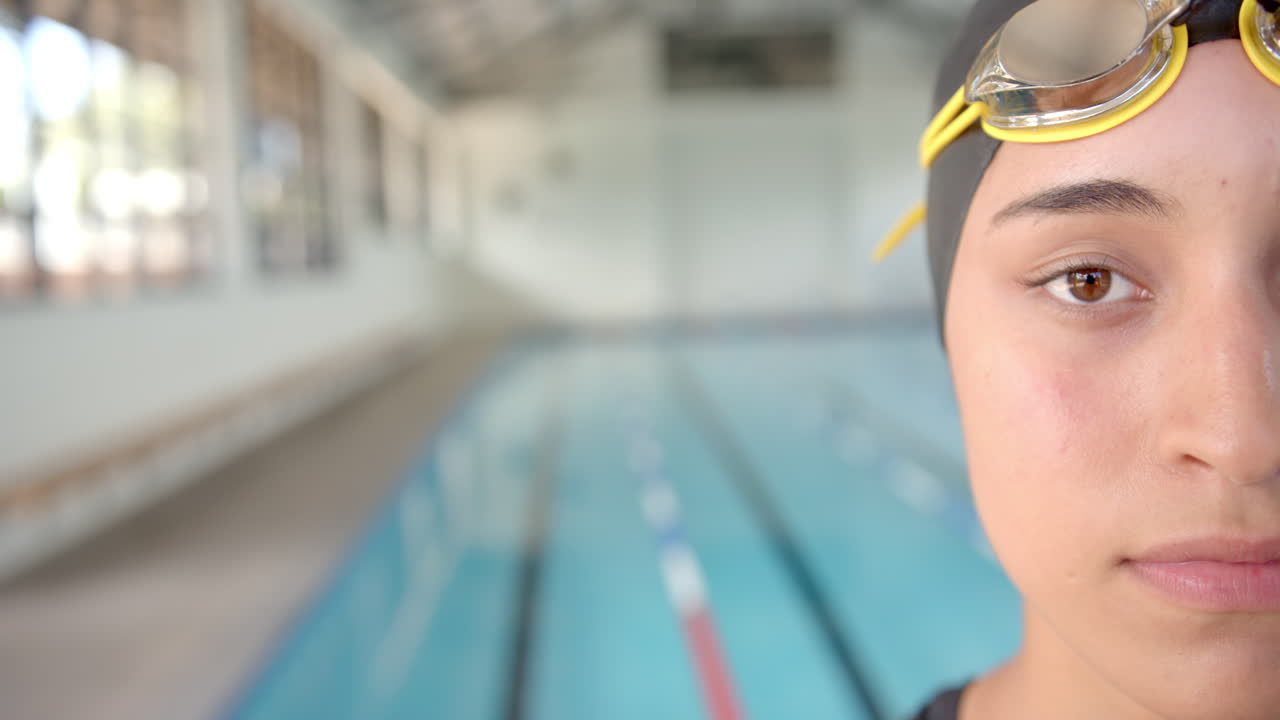 Wearing swim cap and goggles, Female Swimmer standing by indoor pool, ready to swim, copy space