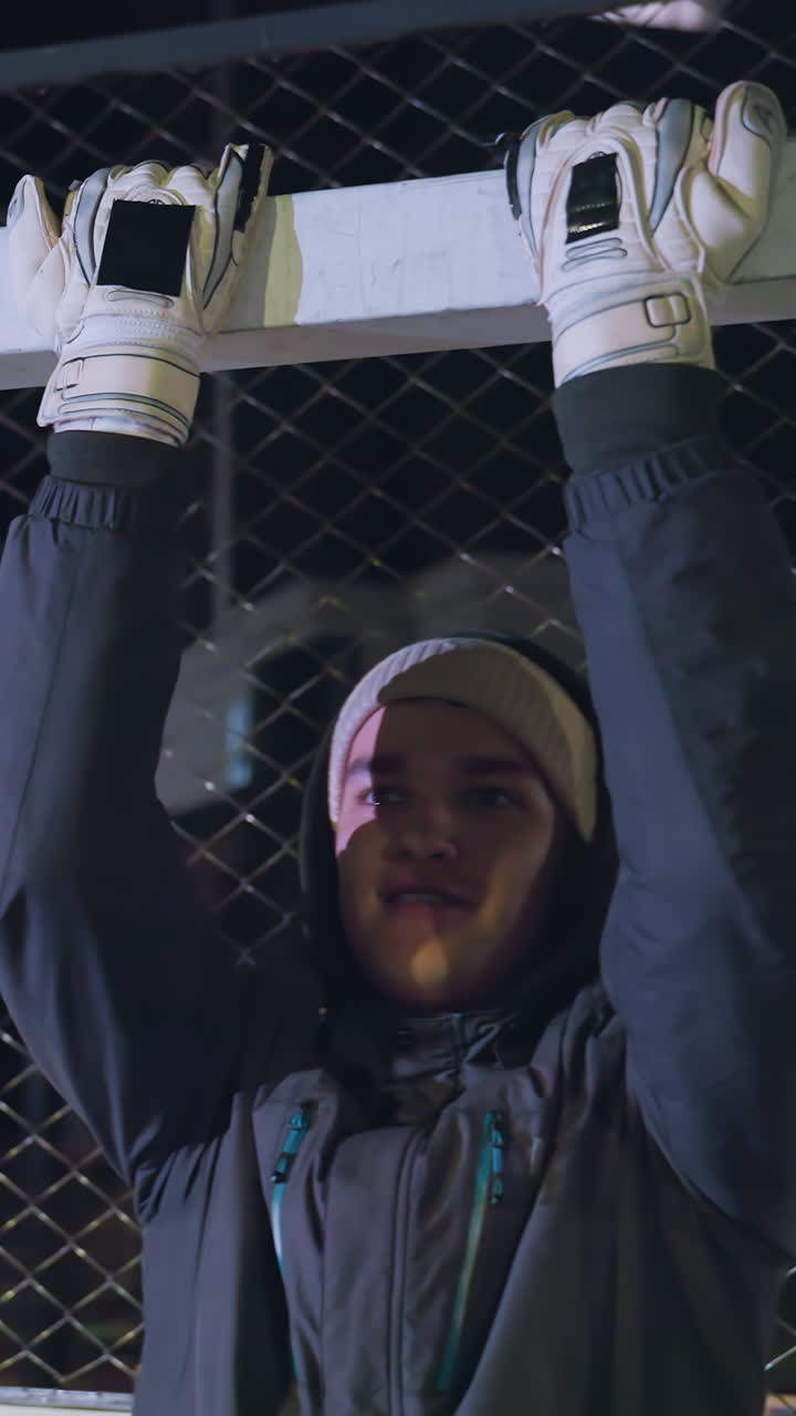 Athlete gripping goal post performing pull-ups during a nighttime training session, showcasing strength and endurance with an illuminated urban backdrop