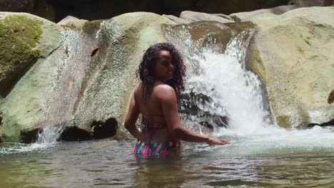 Young-African-girl-in-a-bikini-stands-at-the-base-of-a-flowing-waterfall-in-the-Caribbean