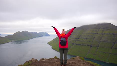 Una-Mujer-Feliz-Levanta-La-Mano-Mientras-Contempla-El-Océano-Desde-La-Cima-De-La-Montaña-Klakkur-En-Las-Islas-Feroe