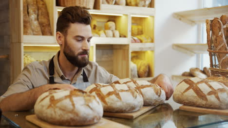 Primer-Plano-Del-Joven-Panadero-Parado-Cerca-Del-Mostrador-En-La-Panadería-Y-Oliendo-Pan-Recién-Horneado