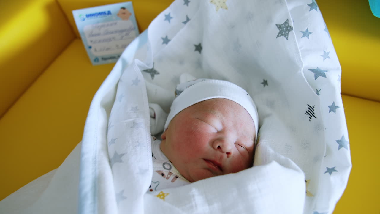 Lovely Caucasian newborn in cap and covered with blankets. Child turns head from a ray of light. Yellow backdrop.