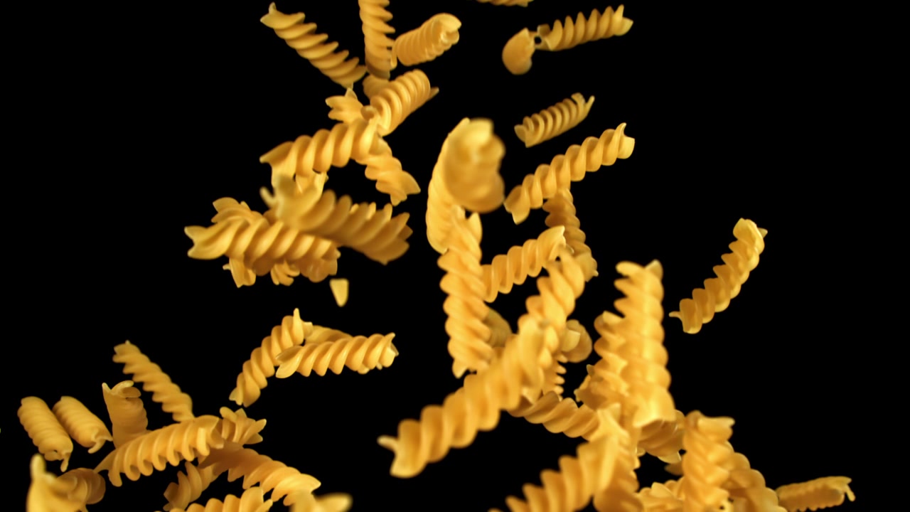 Fusilli che cadono al rallentatore su sfondo nero.