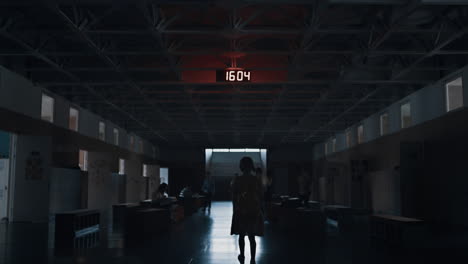 Lonely girl silhouette walking dark corridor to stairway. Pupil passing students