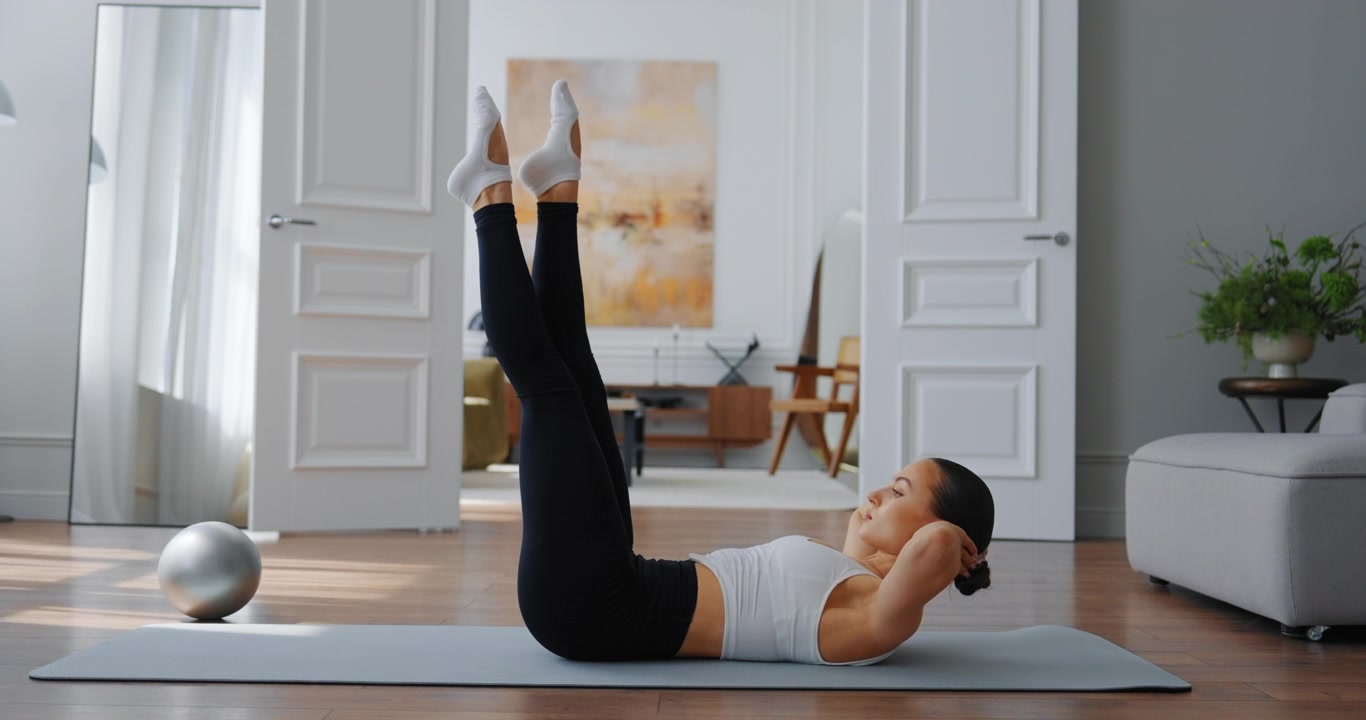 Giovane donna che esegue esercizi di sollevamento gambe su tappetino da yoga a casa