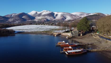 cinematic drone view of keswick by the lake, derwentwater and snowy fells in the background