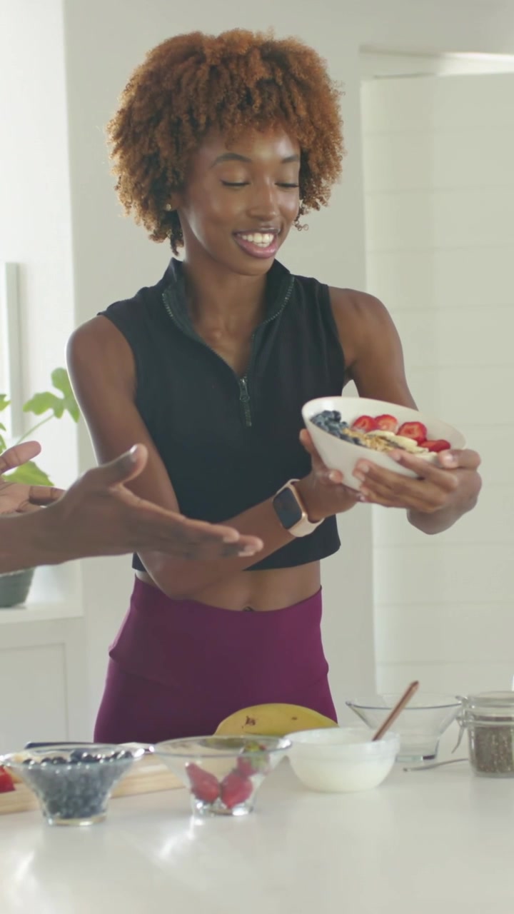 Vídeo vertical: Mulher de top cropped oferecendo uma tigela de frutas vermelhas no balcão, após estender a mão esquerda.