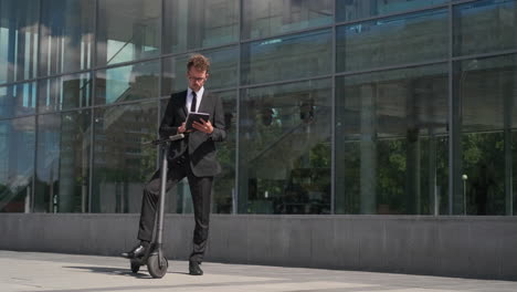 businessman working on a tablet by an electric scooter outside a modern office building