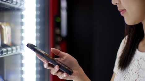 a user engaging with a vending machine displaying snacks while using a smartphone, highlighting modern technology's role in convenient food choices