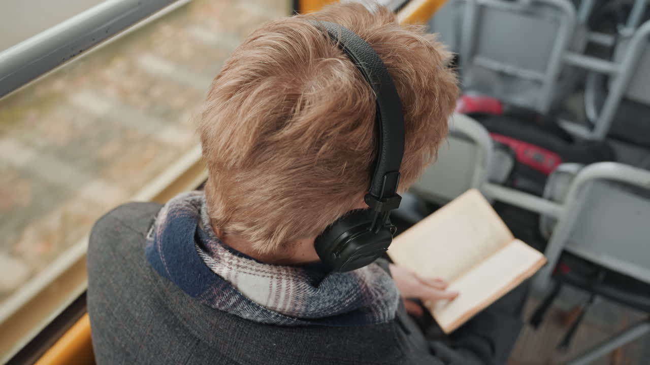 Ung kunstner med bok og hodetelefoner. Tenåringsforfatter studerer romanideer under en fredelig pendlerreise. Ung kreativ person fordypet i lesing og planlegging av historier på offentlig transport.