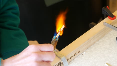 glass jewlry making artisan heats glass with a torch for precision crafting, detailed with hands, flame, and tools on a bench