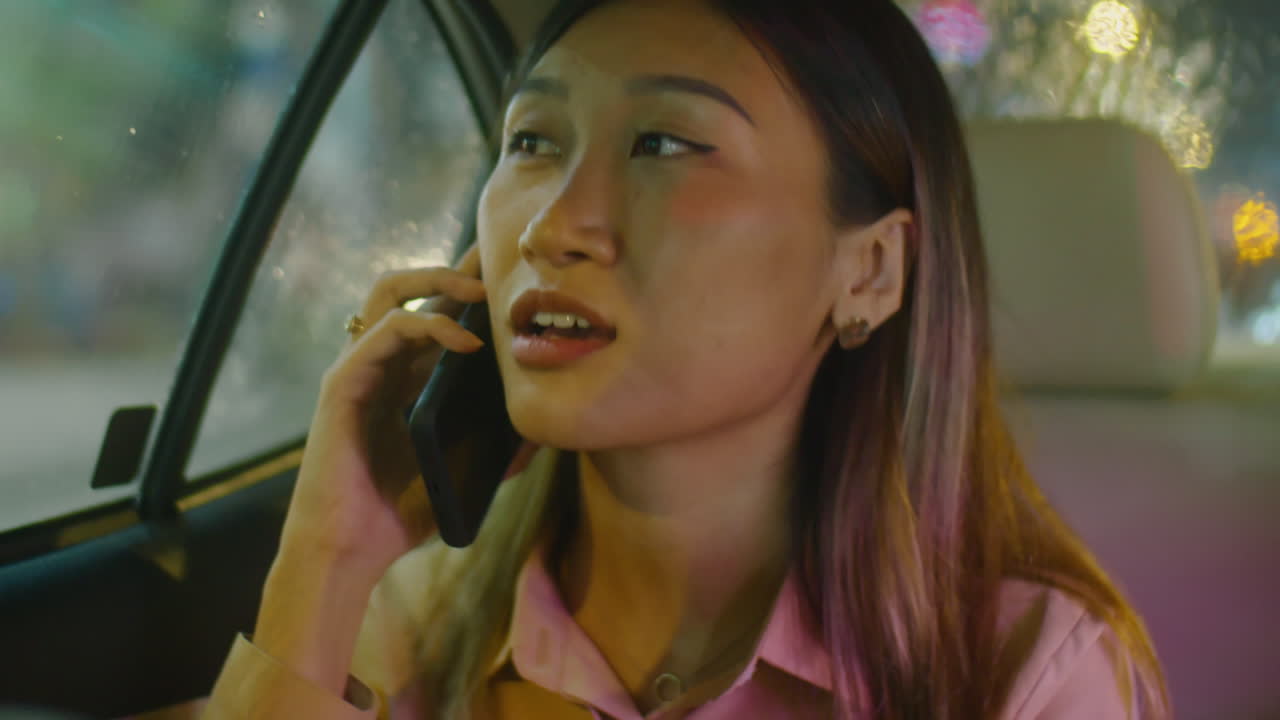 Asian Woman Riding in Taxi at Night and Speaking on Phone