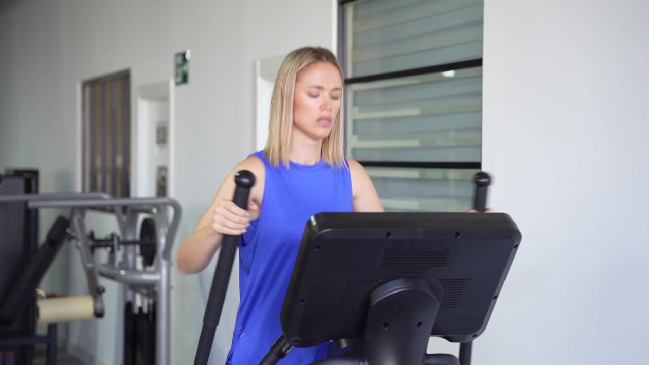 Una donna attiva sull'ellittica in palestra, focalizzata su fitness e benessere.