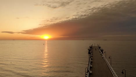 un dron aéreo suave que vuela sobre el mar hacia el sol junto al paseo marítimo de madera