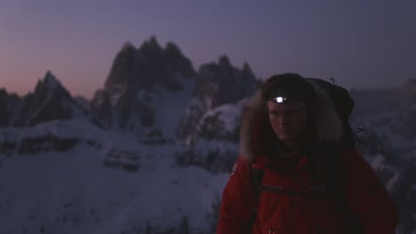 Man-in-red-jacket-walking-up-in-front-of-camera-with-large-beautiful-mountain-in-the-background