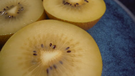 Amazing-close-up-rotating-yellow-kiwi-fruits-on-a-blue-plate,-juicy-tropical-exotic-fruit,-4K-macro-shot