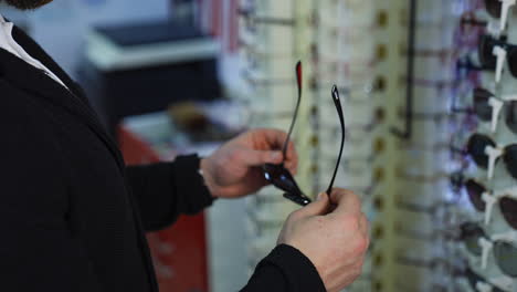showcase with spectacles in modern optics store. man`s hands with glasses. closeup.