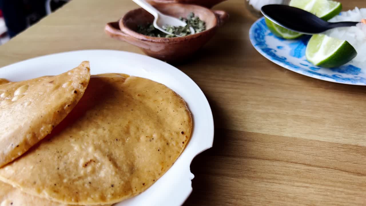 Golden quesadillas are served on a white plate with oregano and lime slices on a wooden table, ready to be enjoyed as a traditional Mexican dish, slow motion reveal