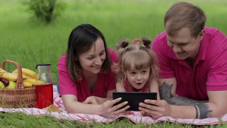 Family-weekend-picnic.-Daughter-child-girl-with-mother-and-father-play-online-games-on-tablet