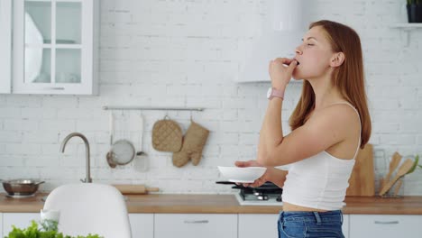 happy girl eats from a plate on a white kitchen background. healthy eating