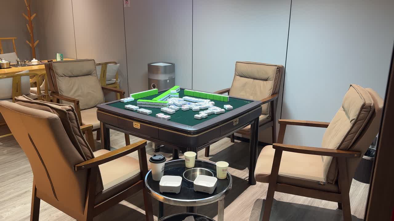 Meja Mahjong disiapkan untuk permainan di dalam lounge Tiongkok modern, menampilkan ubin hijau, kursi kayu, dan suasana dalam ruangan yang santai mewakili tradisi sosial dan budaya rekreasi