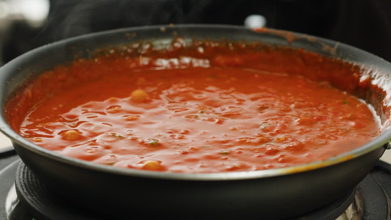 Chicken in tomato sauce is boiling on a frying pan with spices. Cooking tomato sauce curry with chicken fillet. Traditional Italian Mexican Asian dish. High quality studio shot for cafe, restaurant close up.