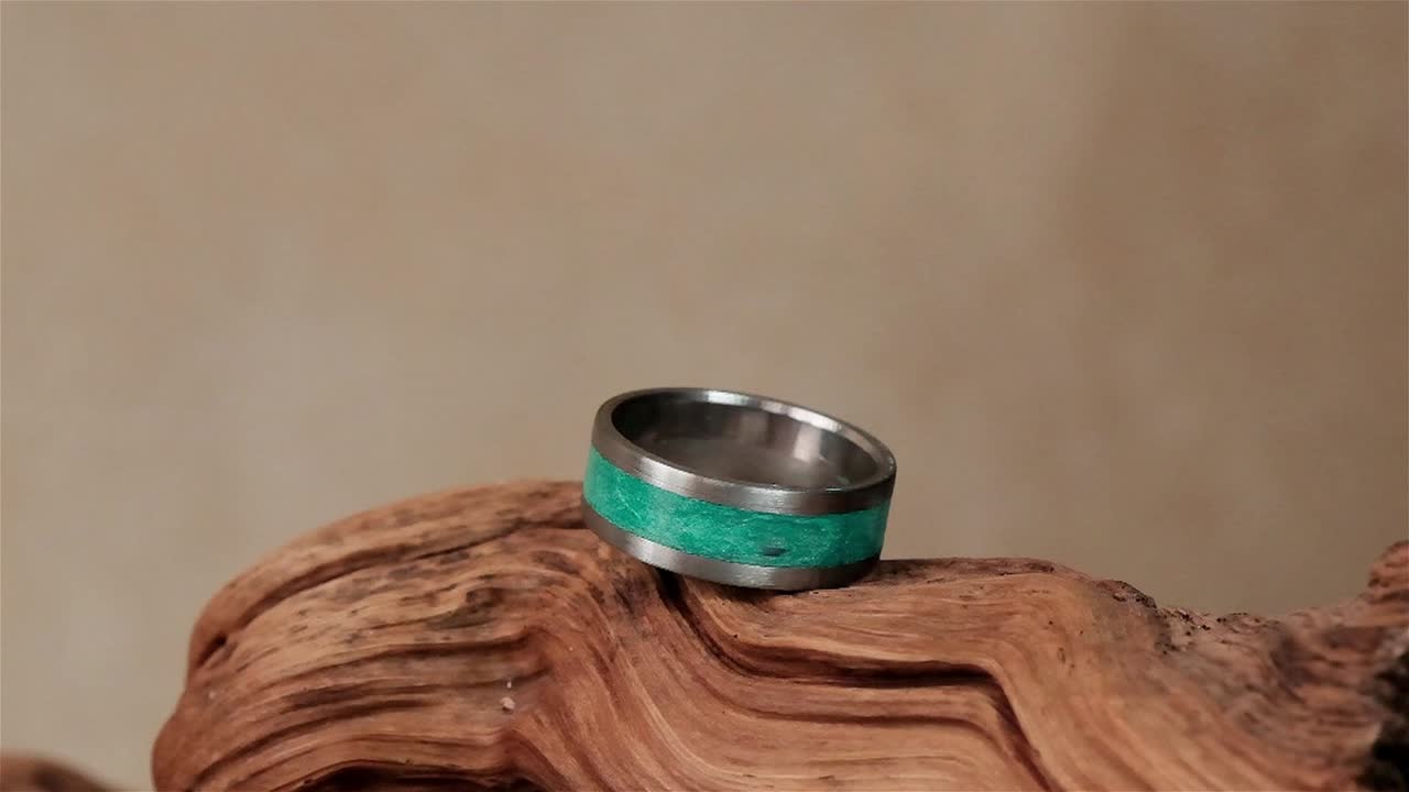 un anillo hecho a mano con acero inoxidable y un núcleo epoxi verde en una pieza de madera para la exhibición